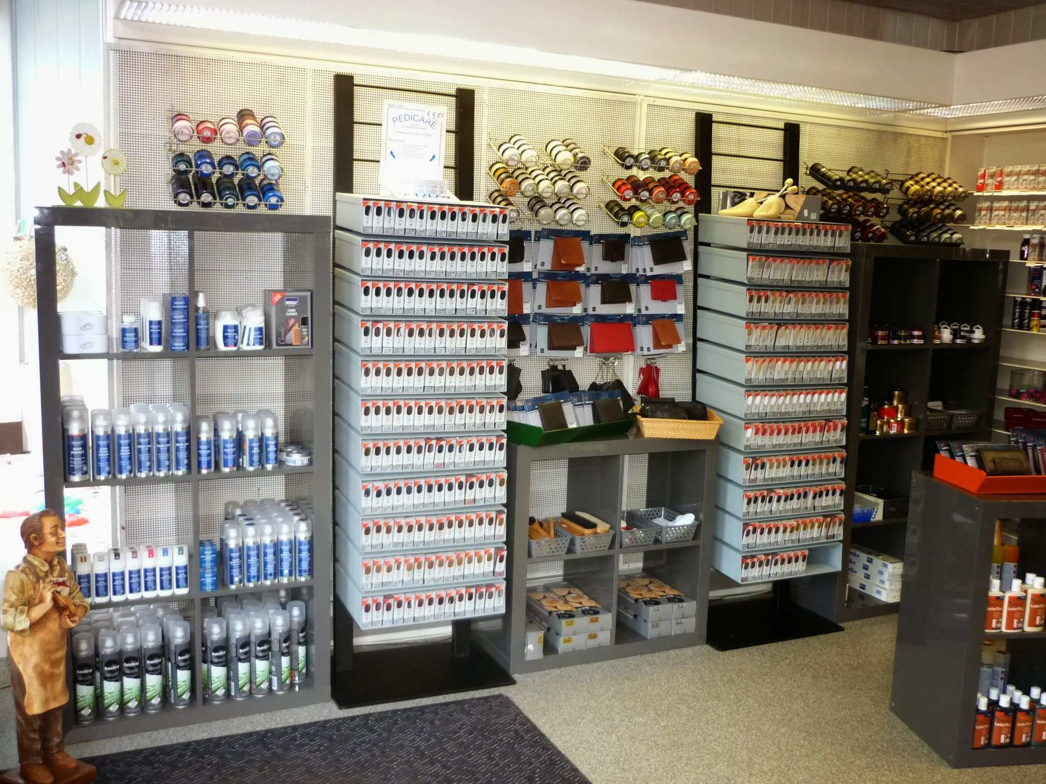 Het interieur van de winkel met onderhoudsmiddelen, lederwaren en een houten schoenmakerfiguur